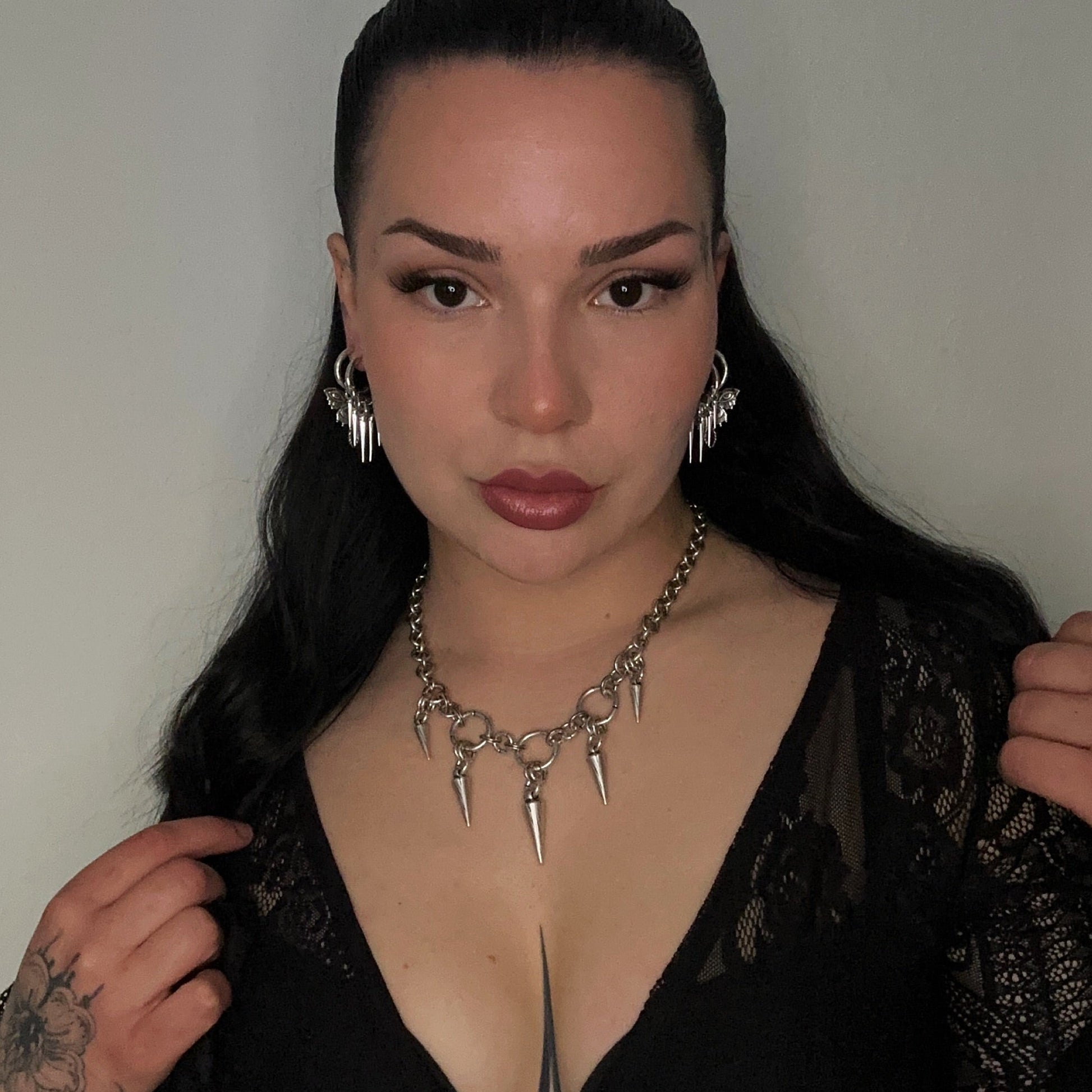 Woman wearing a black lace top with a deep neckline, posing against a plain background.