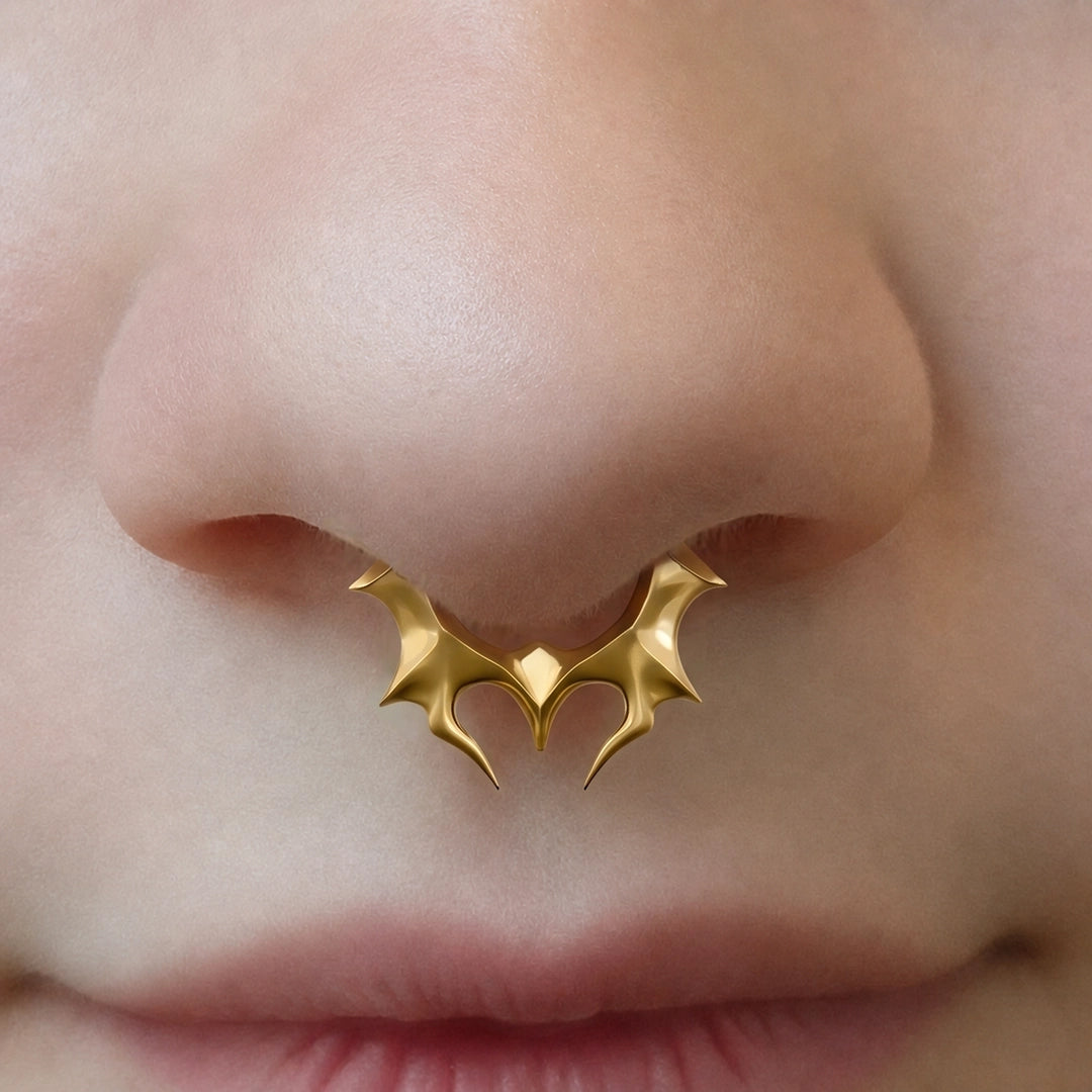 Gold-tone Infernal Horn Clicker worn as a septum ring, showing its dramatic horn-inspired profile.