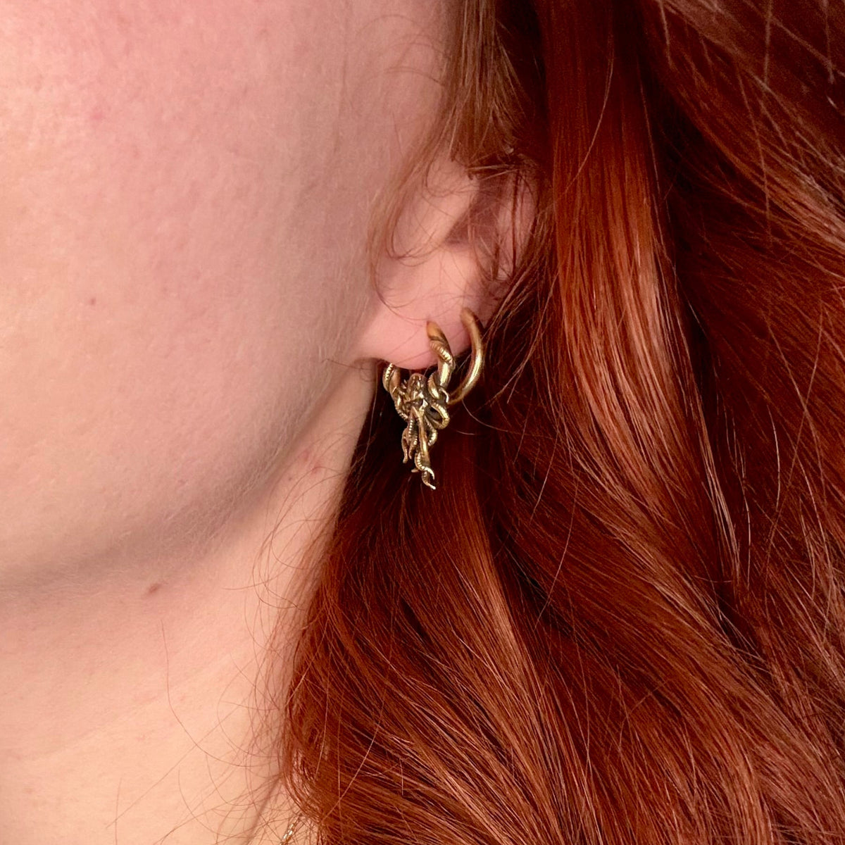 Close-up of a gold-tone kraken hoop earring worn on a model with red hair