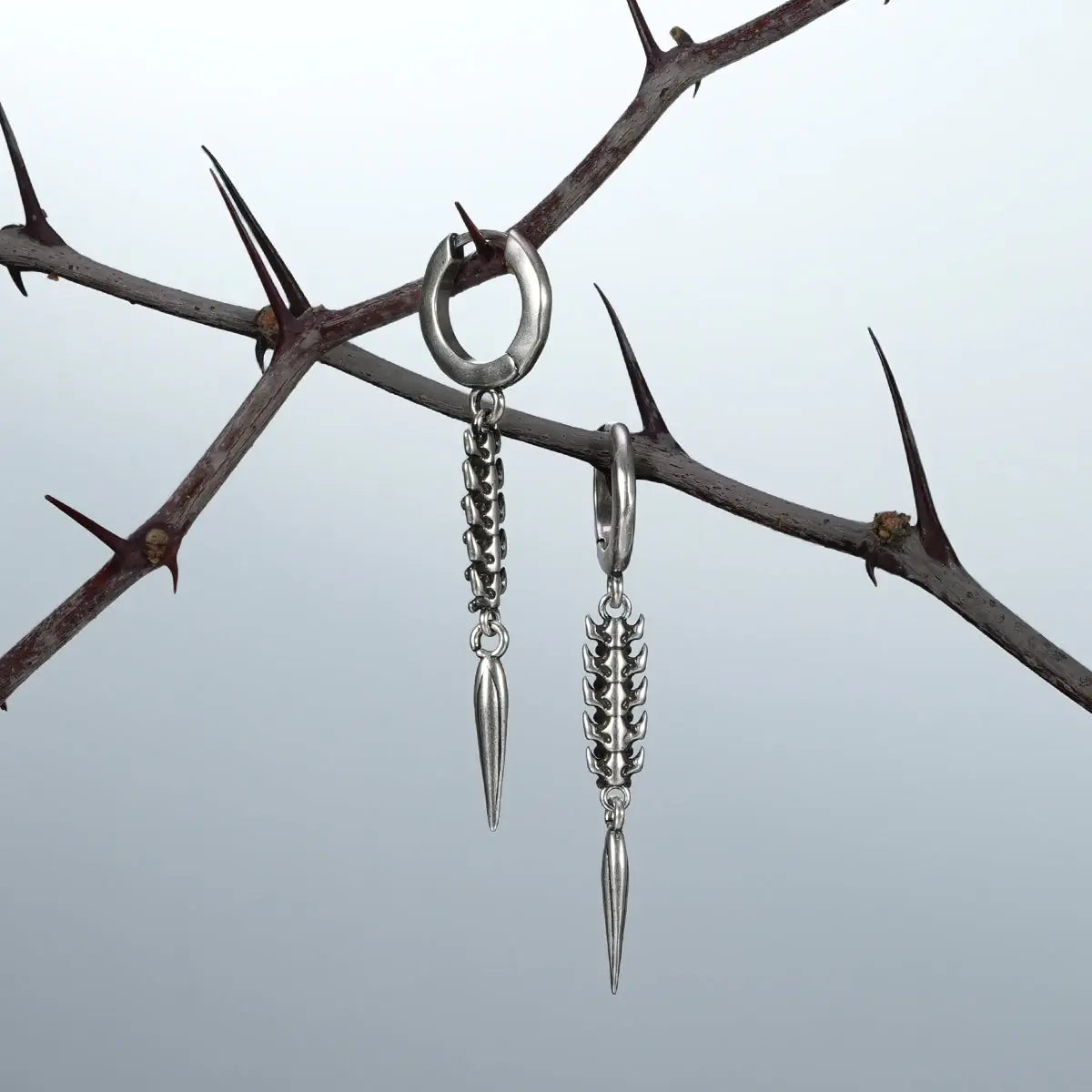 Longinus Abyss Stinger Earrings in 925 sterling silver, pair hanging from thorn branches to highlight the segmented spine tex
