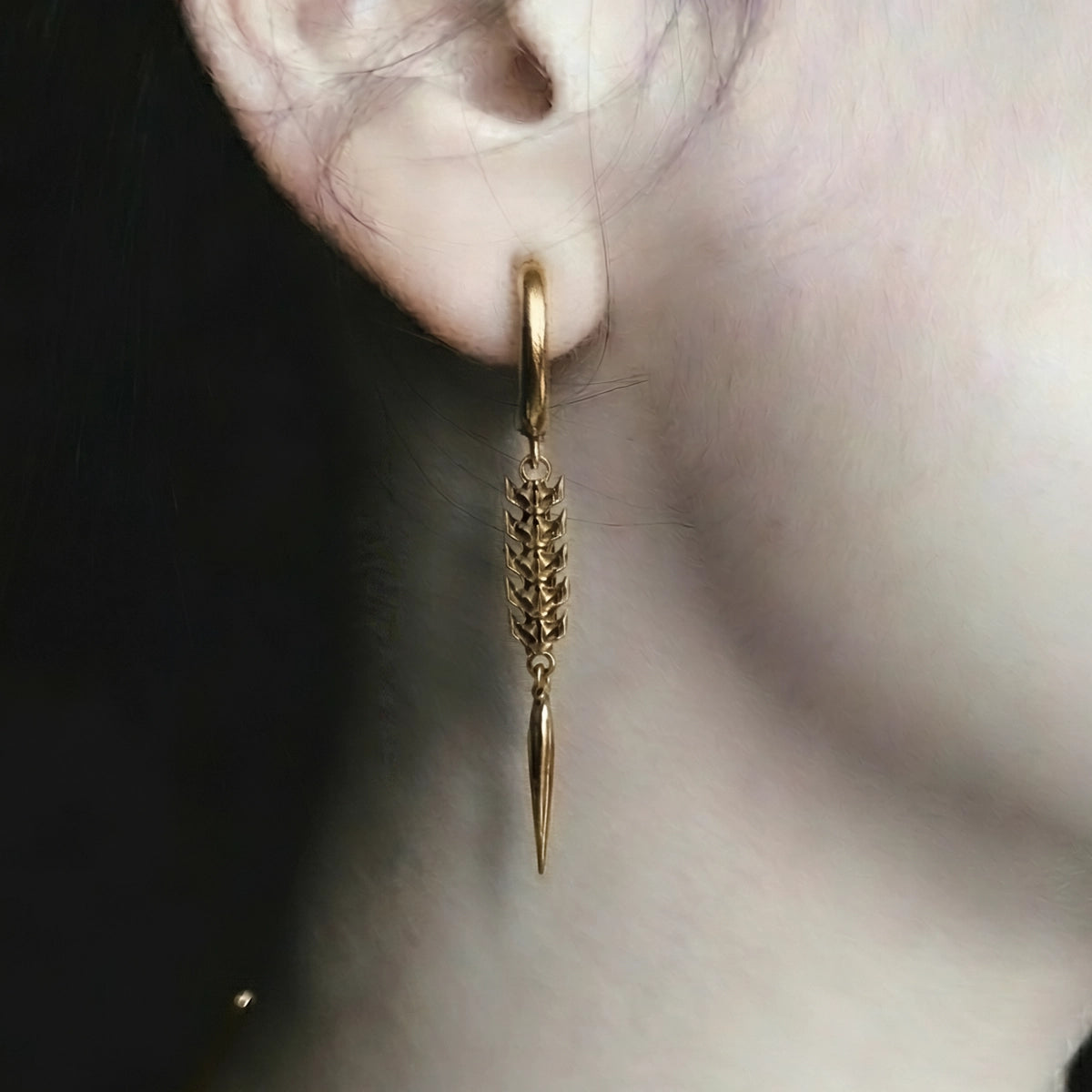 Gold-tone hoop earring with a spine-link drop worn on a model's ear, shown in close-up profile