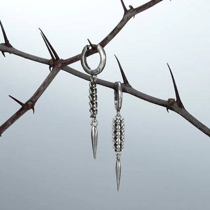 Silver spine and spike drop earrings hanging from a thorned branch against a light background