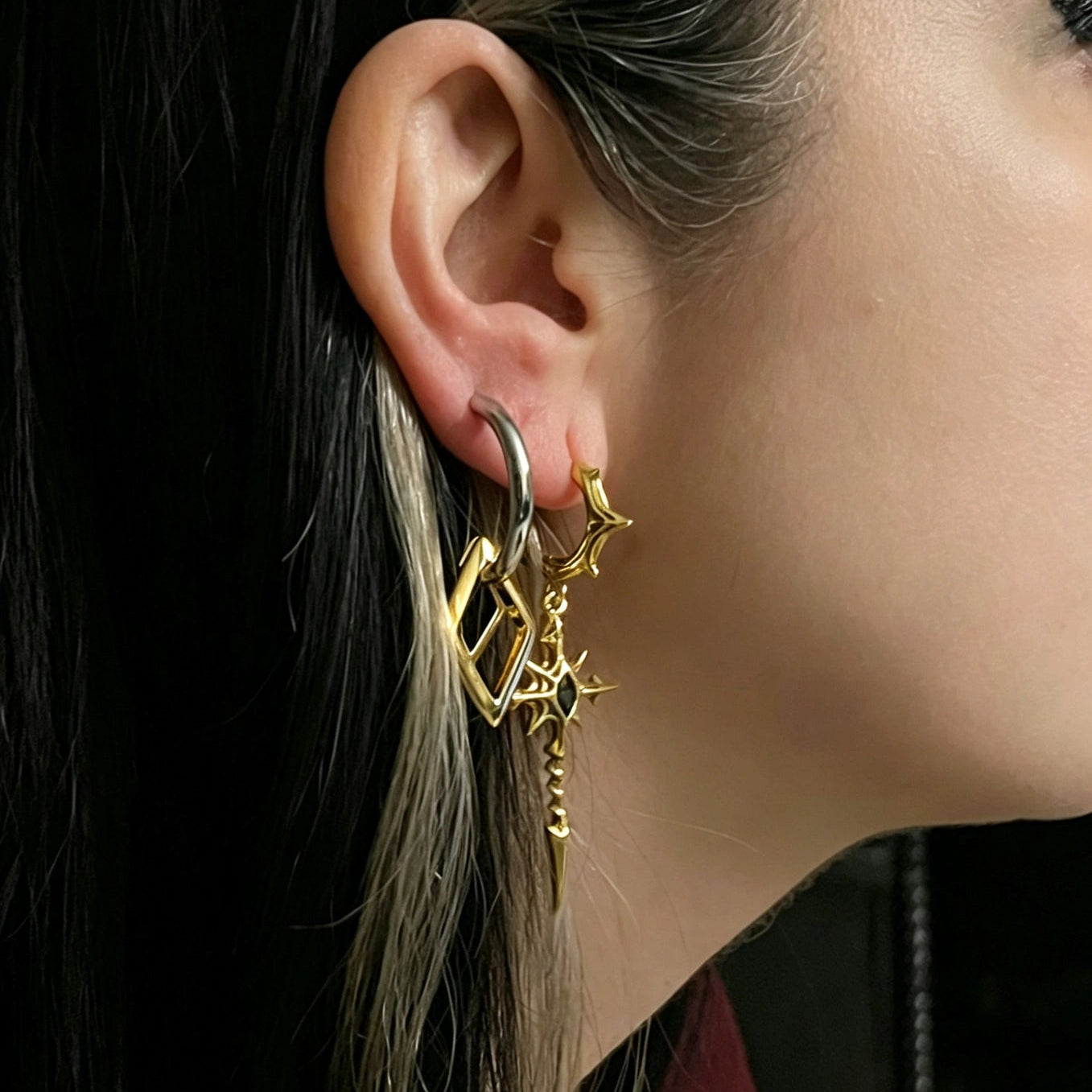 longinus blood relic earrings shown in a close-up model view, featuring gold gothic spear drop earrings with a red center stone worn on the ear