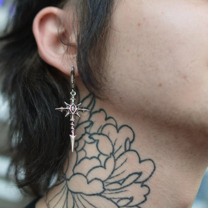 longinus blood relic earrings shown in a model close-up view, featuring a silver cross-shaped drop earring with a red gemstone detail worn on the ear