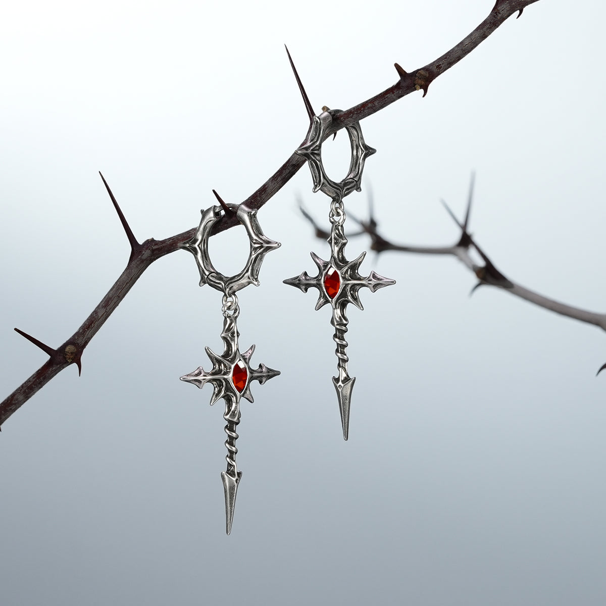 Pair of silver Longinus Blood Relic earrings with red center accents on thorns