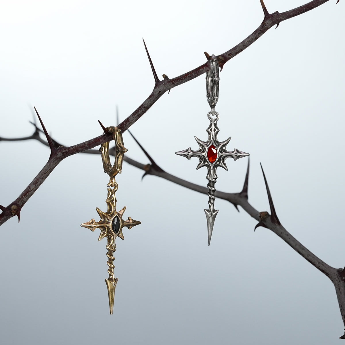 Gold and silver Longinus Blood Relic earrings hanging from a thorn branch