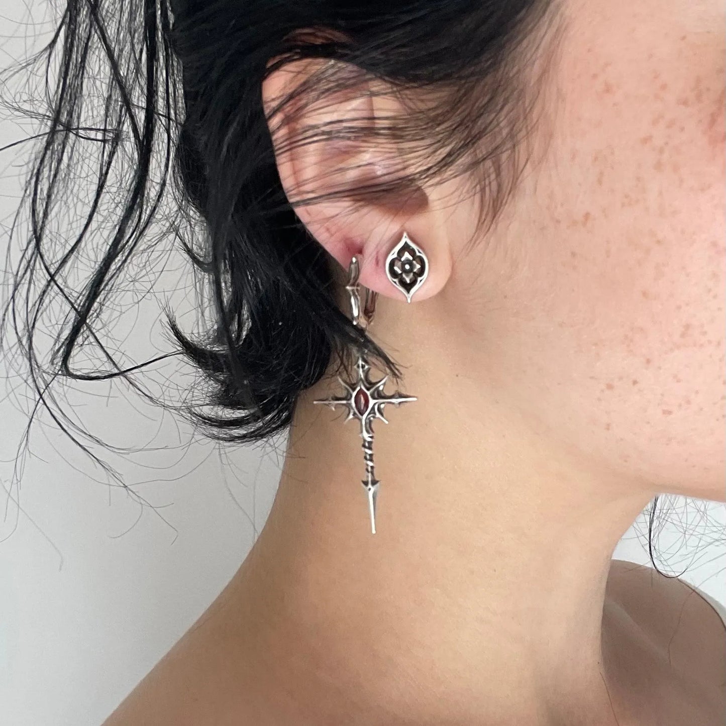 Model wearing silver Longinus Blood Relic Earrings with crimson core and long gothic spear drop design