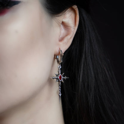 Side profile of a model wearing a silver-tone cross dagger earring with red gemstone accent