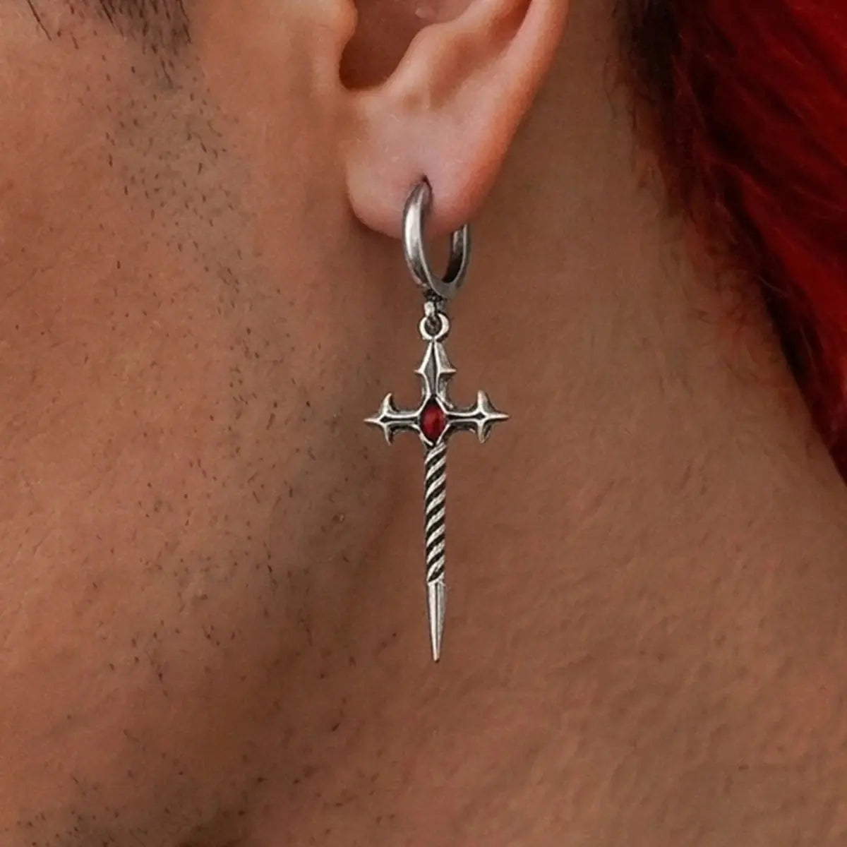 Longinus Godpiercer Earrings in 925 sterling silver, worn in a clean ear close-up on medium skin, showing the red stone and t