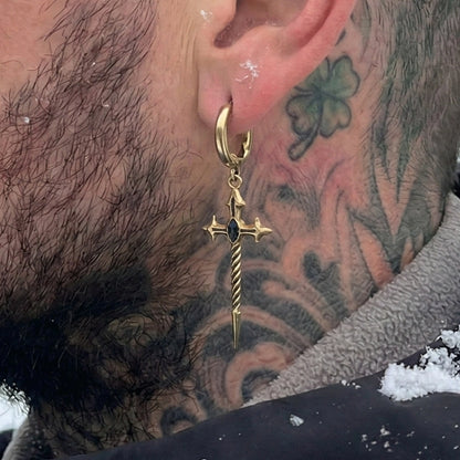 Gold-tone Longinus Godpiercer hoop earring with a sword drop worn beside a tattooed neck