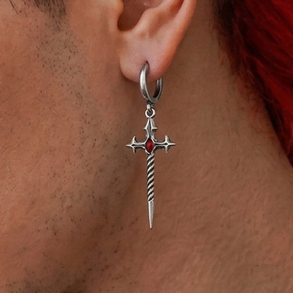 Sword-shaped dangle earring with a red stone hanging from a hoop, worn close-up on an ear