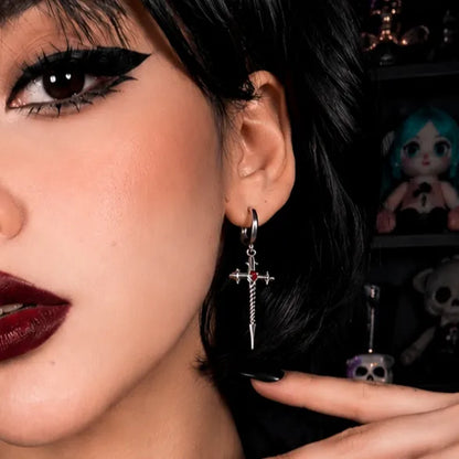 Model wearing the silver Longinus Godpiercer Earrings with red stone centers, cross-like blade details, and dark gothic styling.