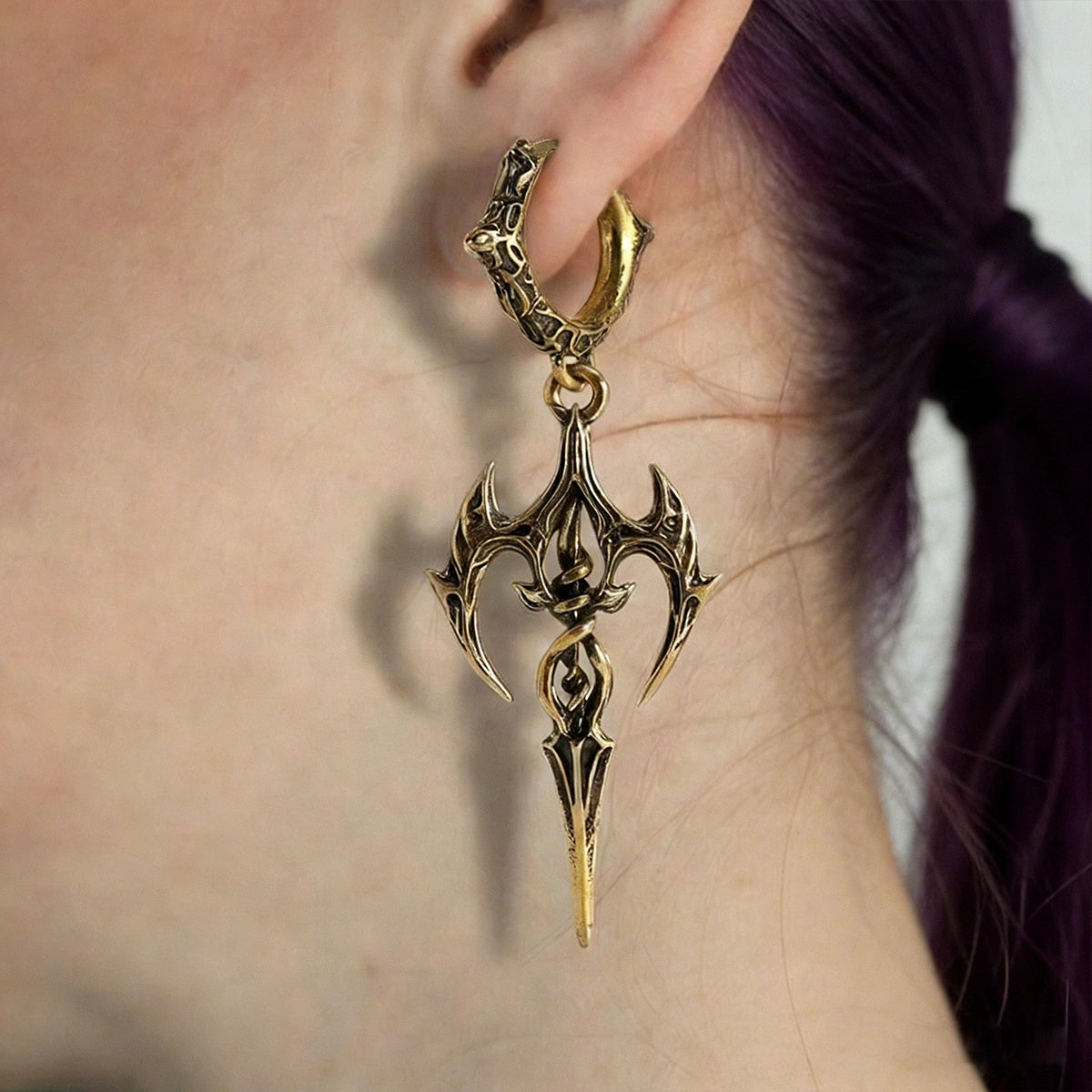 Antique gold-tone halo earring with a spear-shaped pendant worn on a model's ear against dark hair