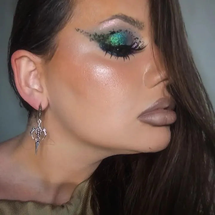 Close-up of a woman's face with glittery eye makeup and an earring.