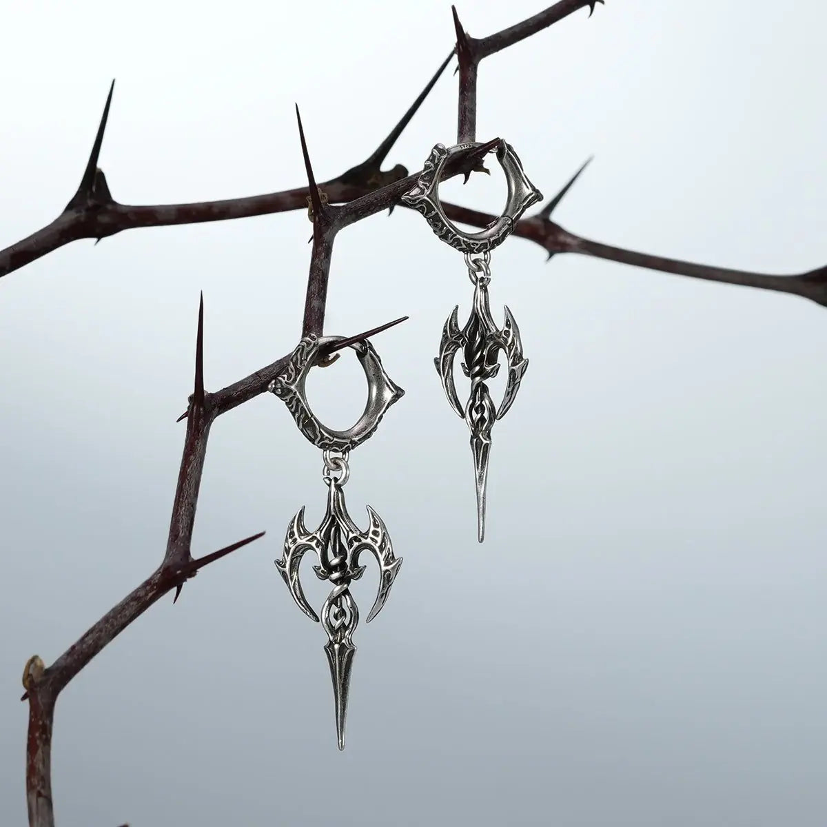 Silver Longinus Halo Piercer earrings hanging from dark thorn branches