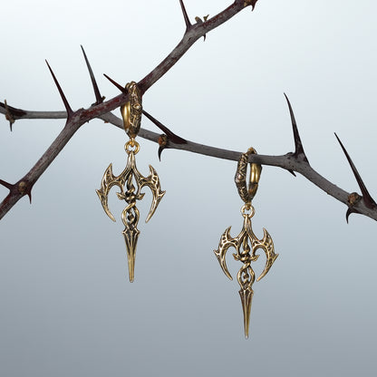 Gold Longinus Halo Piercer earrings displayed on dark thorn branches