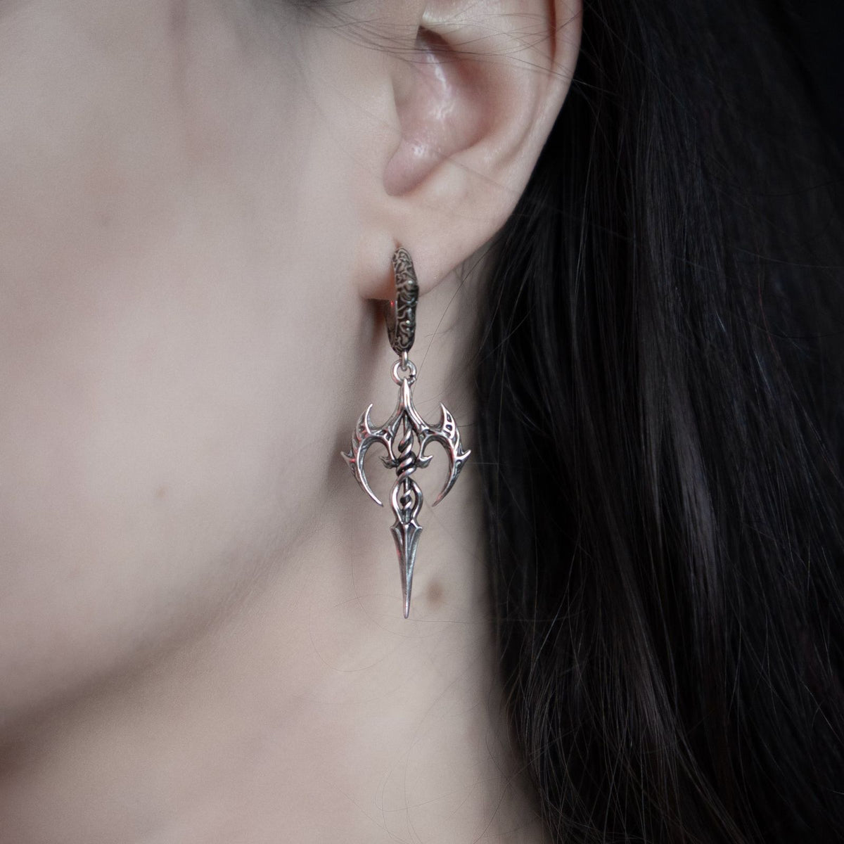 Silver-tone halo piercer earring with a spear-like gothic pendant worn on a model's ear, close-up view