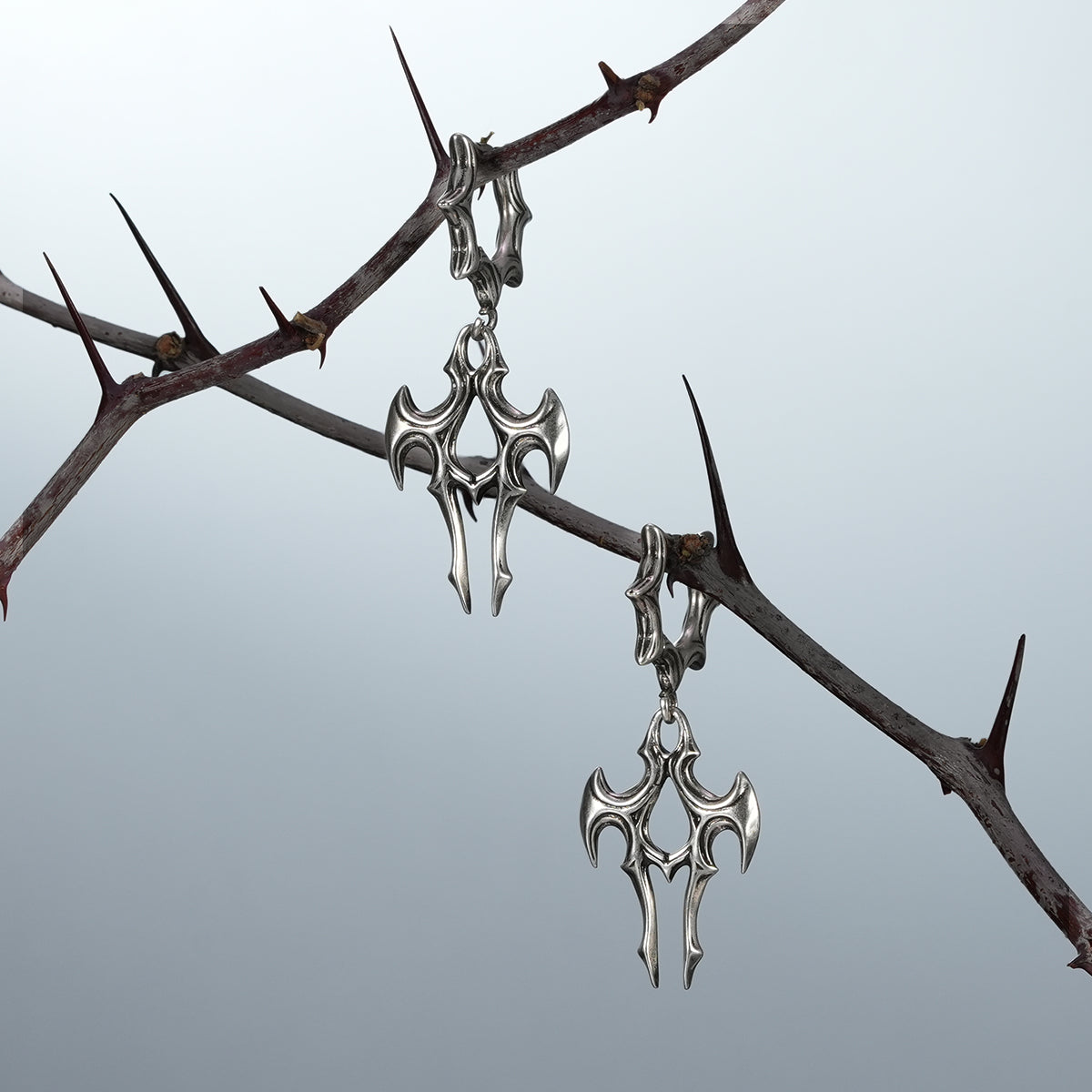 Pair of silver Longinus Judgment Talon earrings hanging from thorn branches