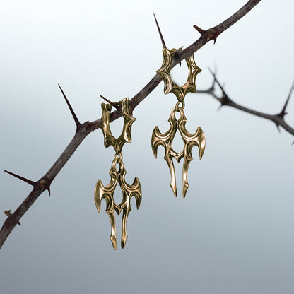 Pair of gold Longinus Judgment Talon earrings hanging from a thorn branch