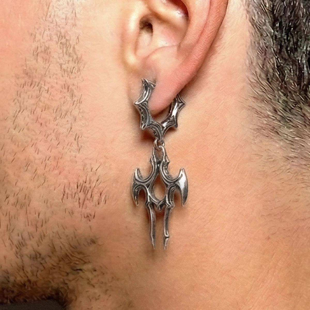 Silver-tone talon drop earring on a spiked hoop worn close to a bearded jawline
