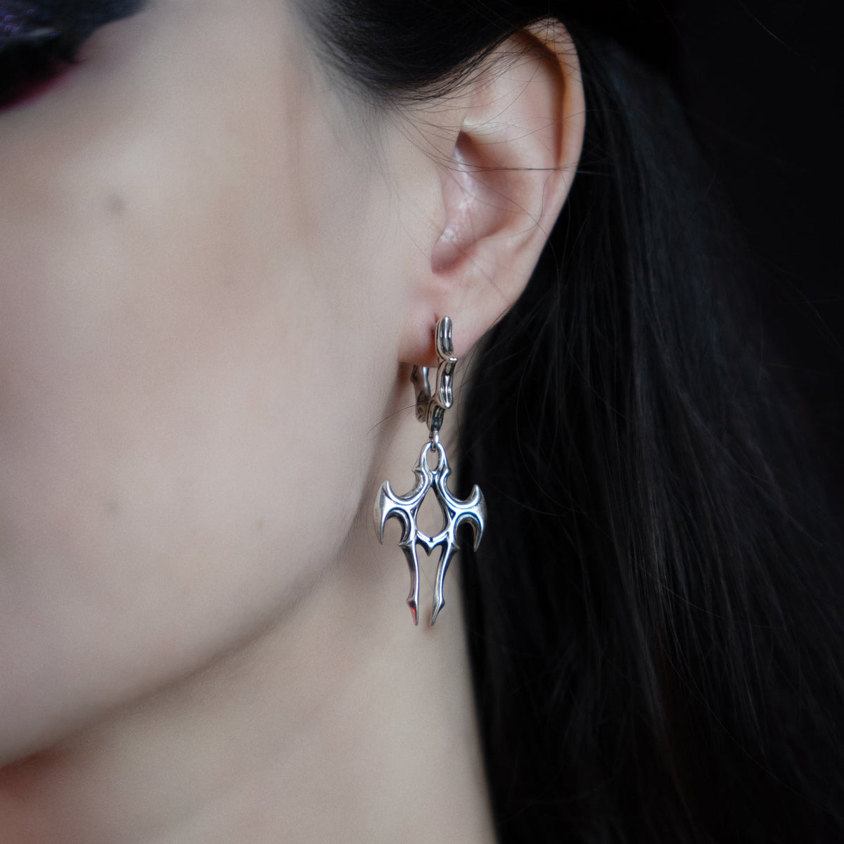 Close-up of a silver-tone talon drop earring worn on a spiked hoop, seen from the side profile