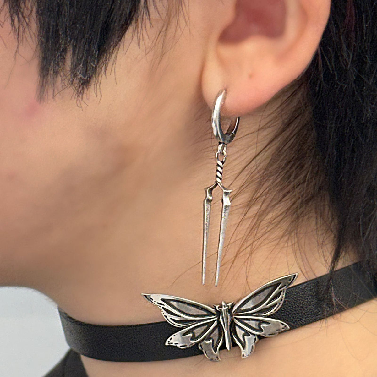 Longinus Twin Spear Earrings in 925 sterling silver, worn in a close side view above a black choker with a silver butterfly o