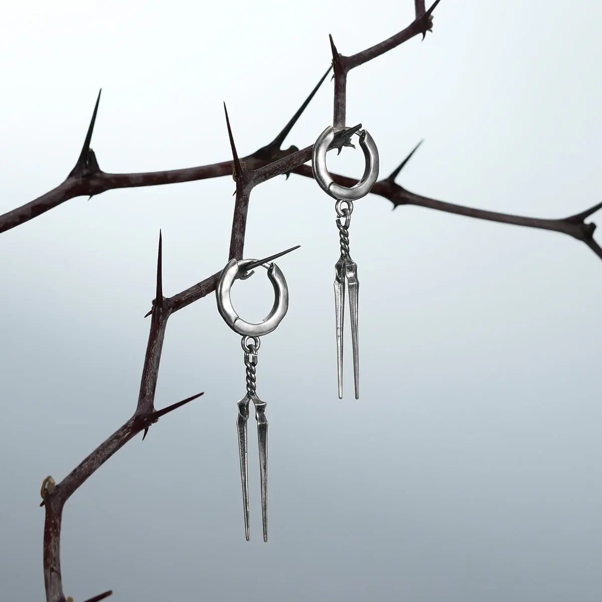 Longinus Twin Spear Earrings in 925 sterling silver, pair hanging from thorn branches to emphasize the long twin-spear silhou