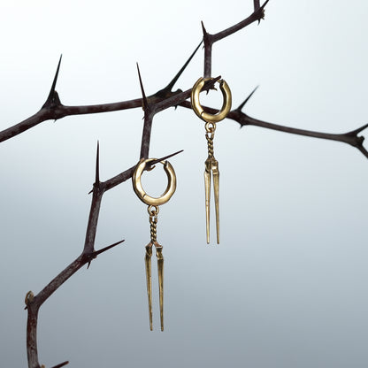 Two gold-tone Longinus Twin Spear hoop earrings hanging from dark thorn branches