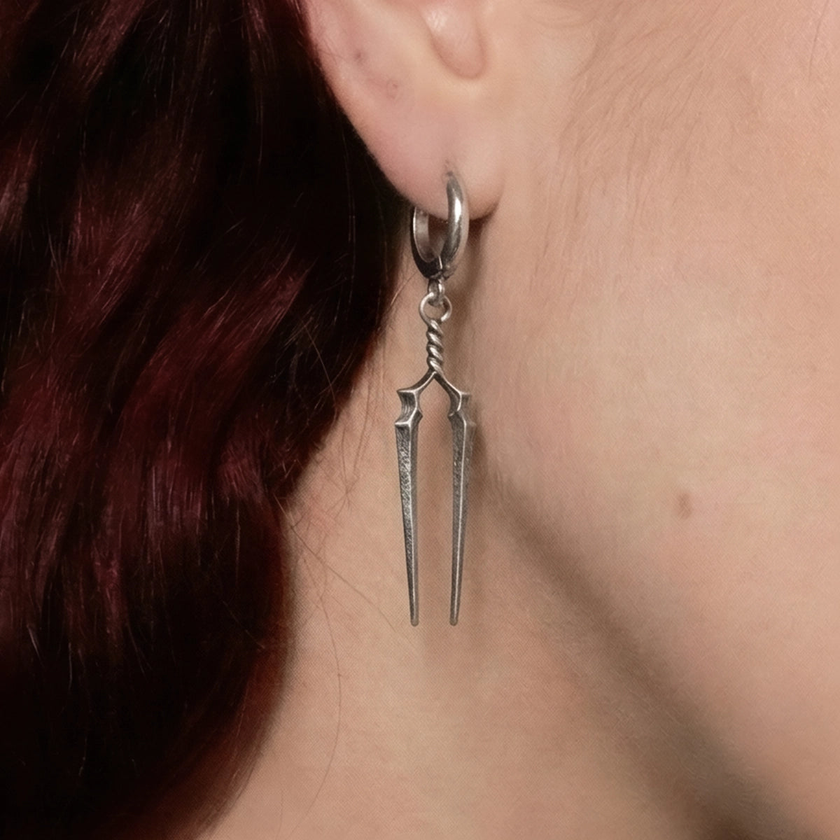 Silver-tone hoop earring with twin spear-shaped drops worn on a model, close-up side view