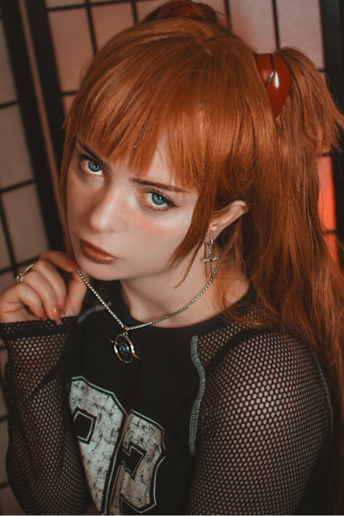 Person with red hair styled in pigtails wearing a black outfit with mesh sleeves.
