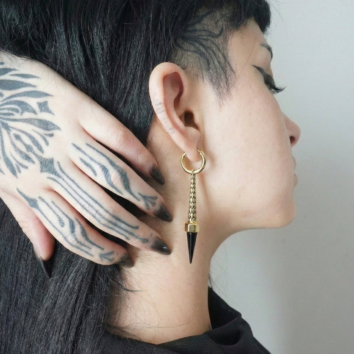 Model wearing a gold-tone hoop earring with chain and dark spike pendant, side view