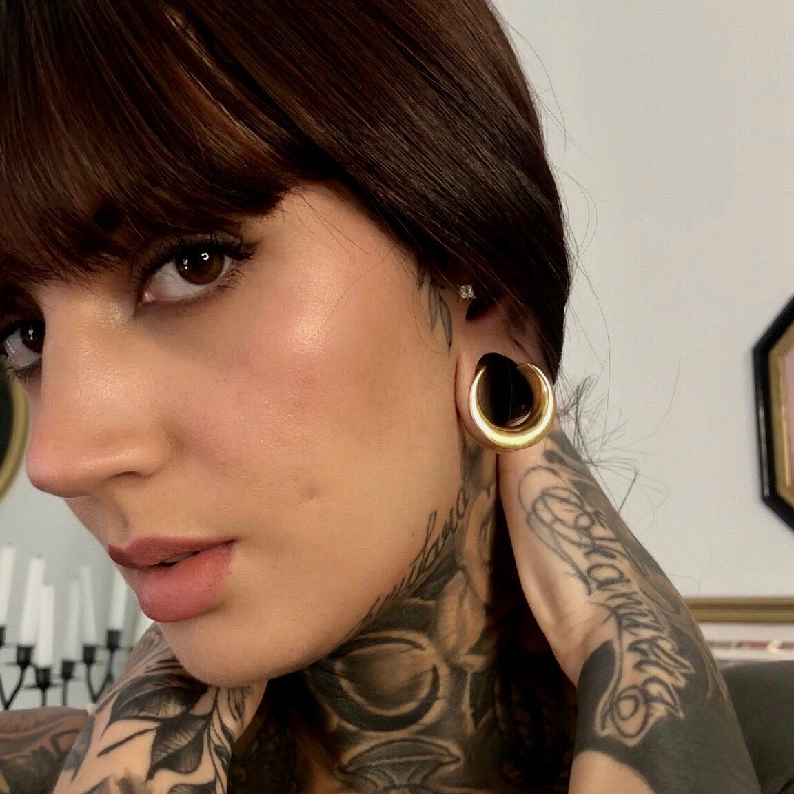 Model with dark hair wearing a gold-tone crescent ear tunnel visible through a stretched lobe