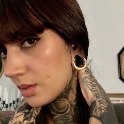Model with dark hair wearing a gold-tone crescent ear tunnel visible through a stretched lobe