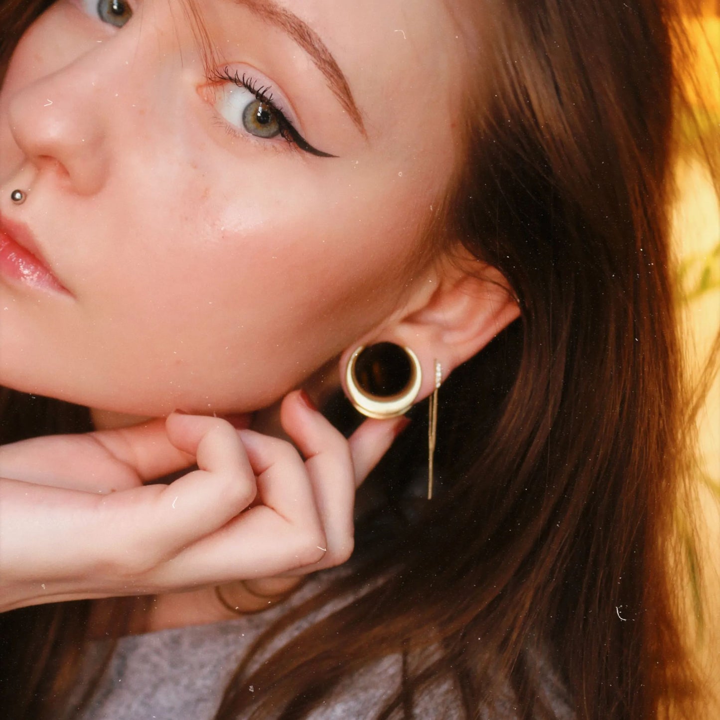 Close-up of a model wearing a gold-tone crescent ear tunnel with a thin dangling gold-tone chain earring