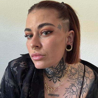 Model with tattoos wearing a gold-tone crescent ear tunnel alongside multiple ear piercings and a chain necklace