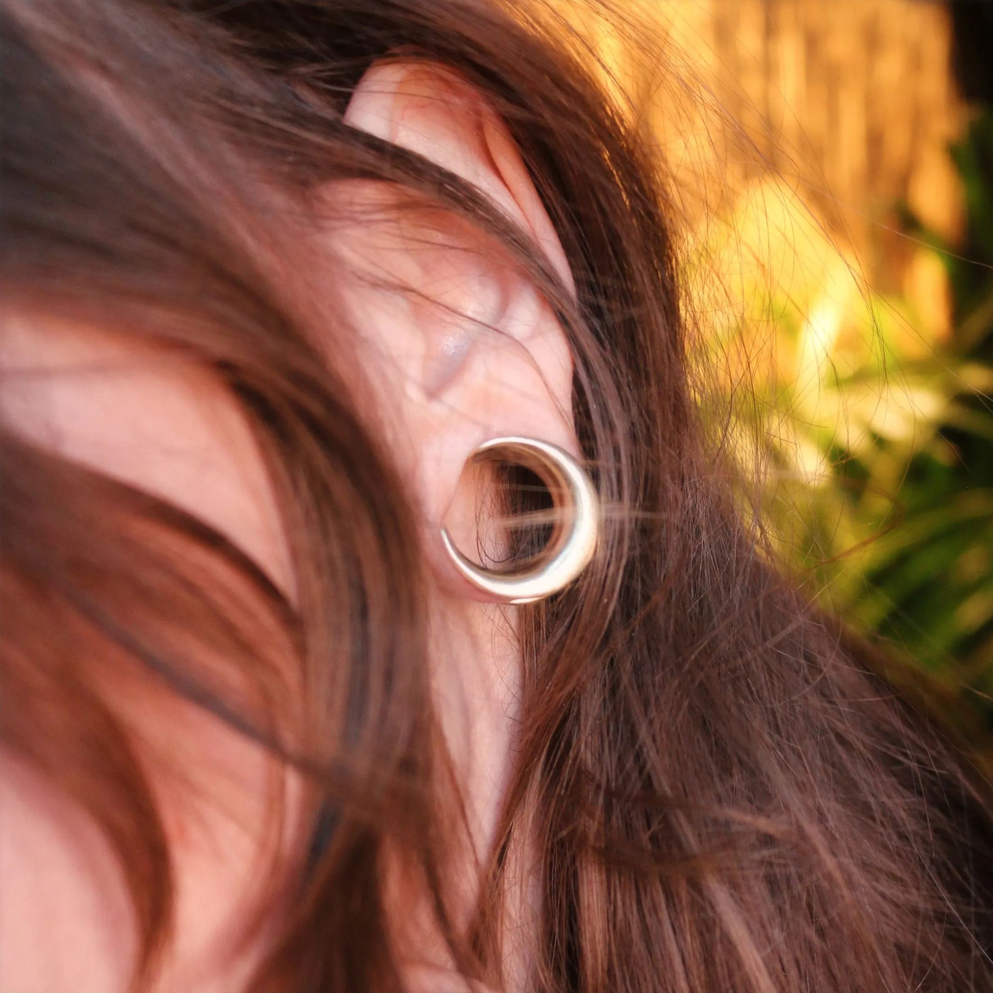 Close-up of a model's ear showing a silver-tone crescent tunnel through the lobe