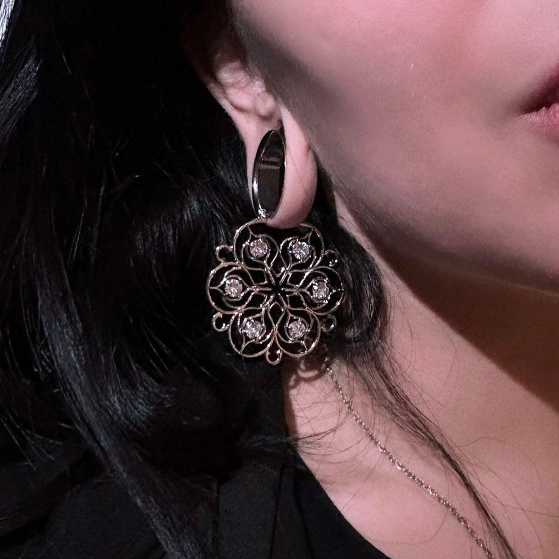 Silver-tone Mandala Bloom earring worn with a black ear tunnel, close view of the circular floral design