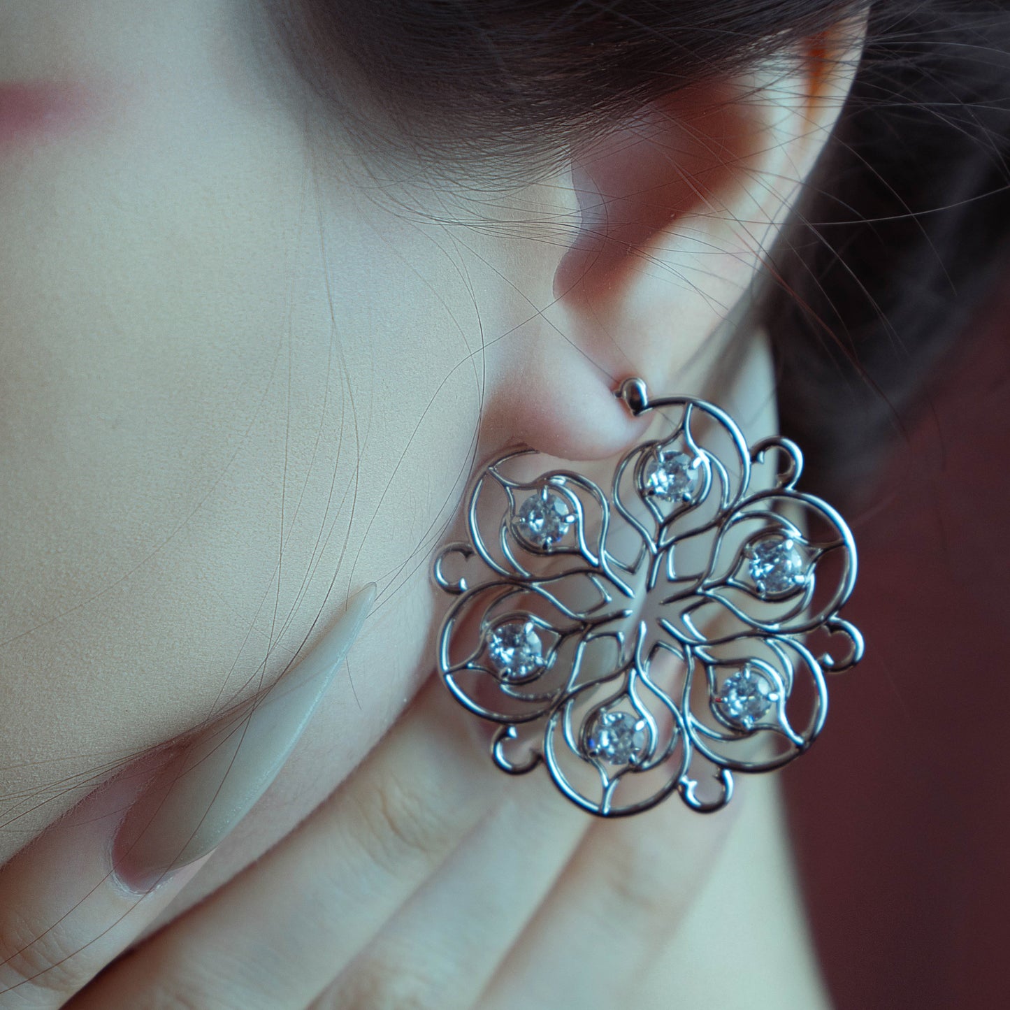 Silver-tone Mandala Bloom earring held beside an ear, showing the open floral pattern and clear stones