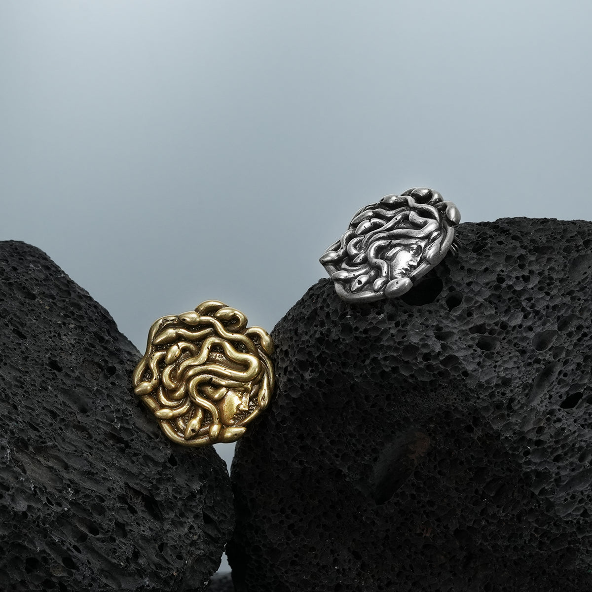 medusa unbound brooch shown in a product view on black volcanic rock with the gold front and silver back, featuring a sculpted medusa face design and pin closure