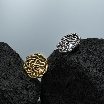 medusa unbound brooch shown in a product view on black volcanic rock with the gold front and silver back, featuring a sculpted medusa face design and pin closure