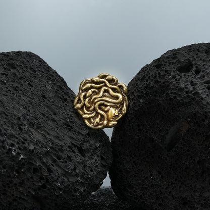 medusa unbound brooch in gold shown in a product view on black volcanic rock, featuring a sculpted medusa face formed by flowing snake details