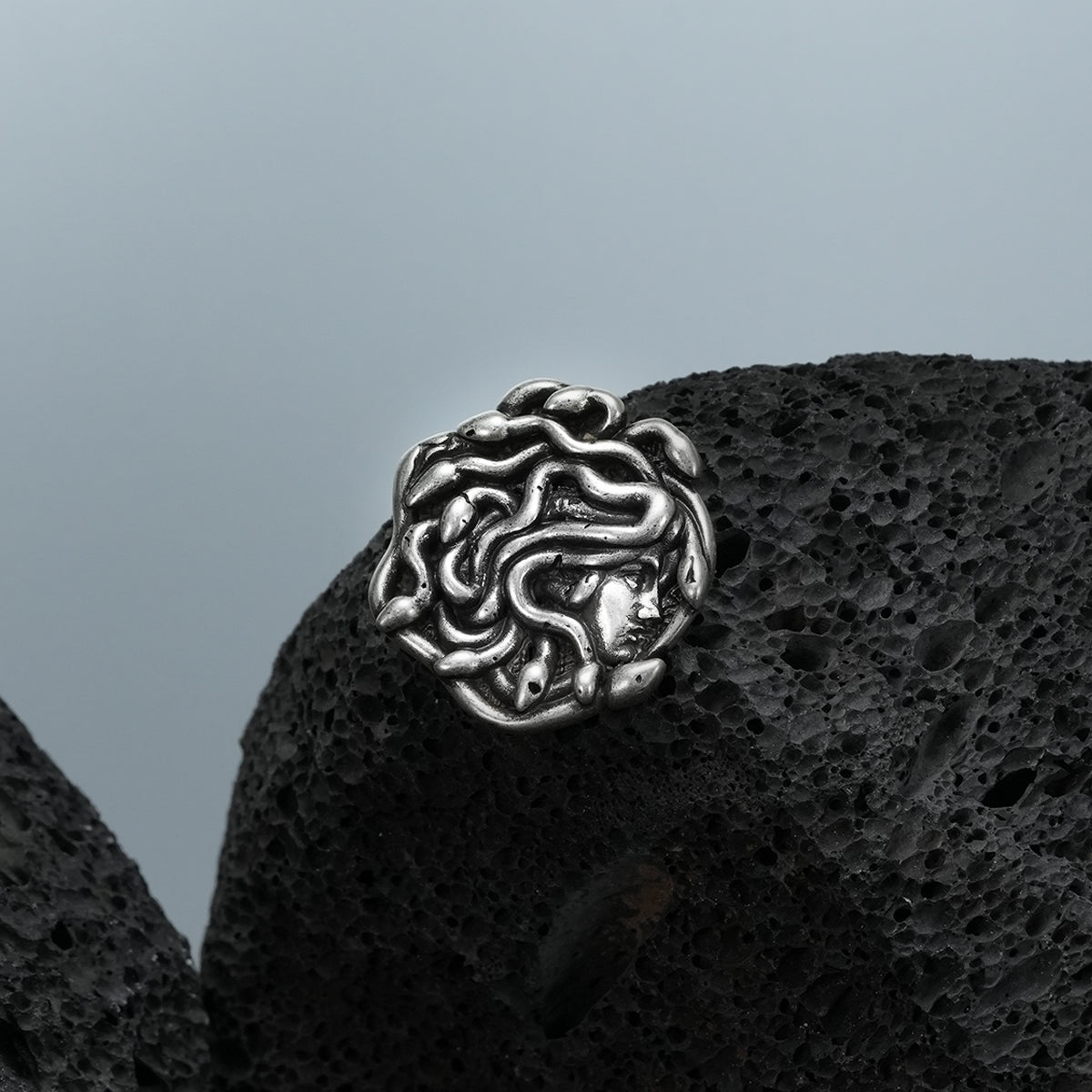 medusa unbound brooch in silver shown in a product view on black volcanic rock, featuring a sculpted medusa face formed by flowing snake details