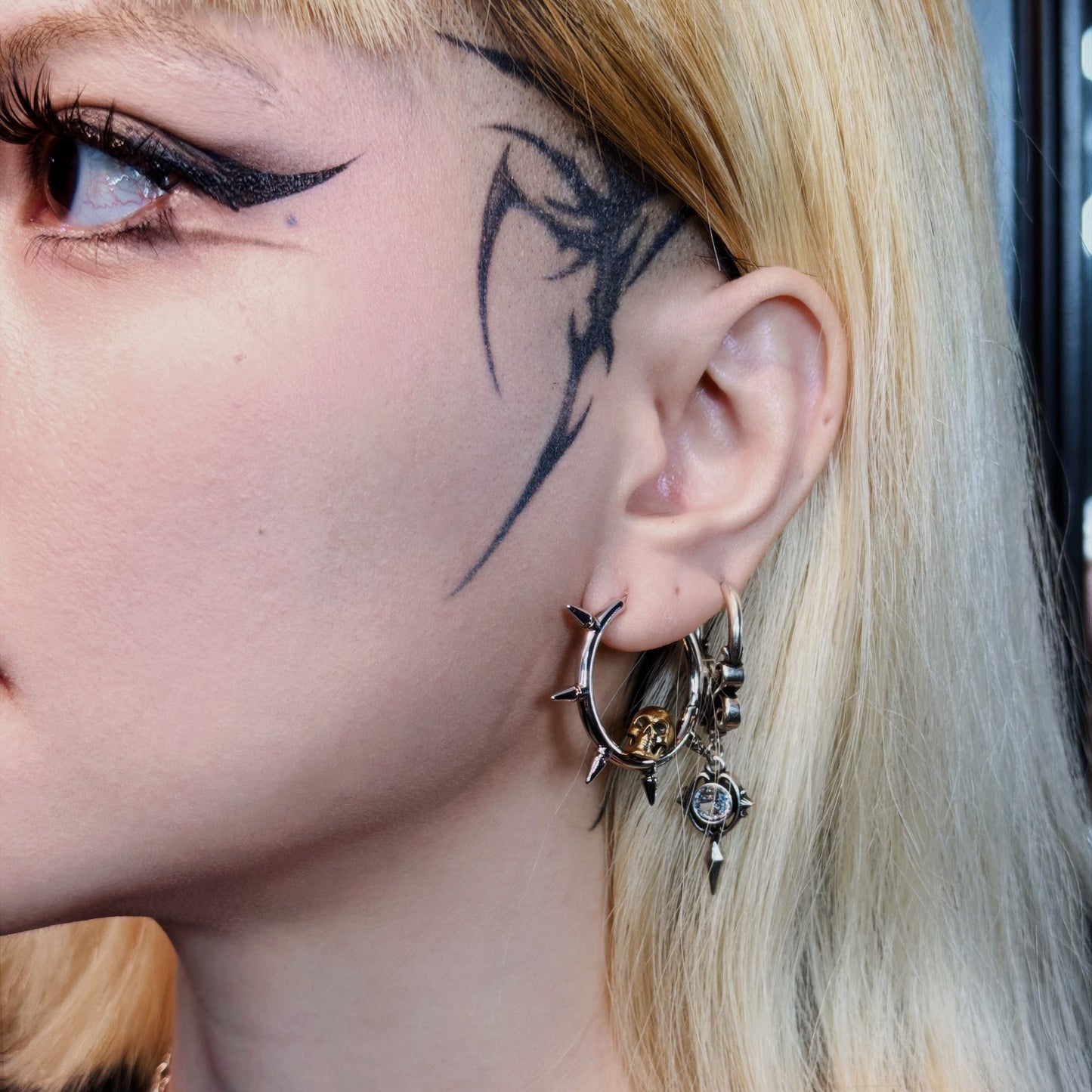 Close-up of model wearing a spiked hoop earring with skull charm and dangling chain earrings