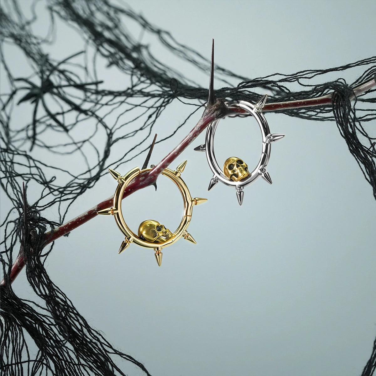 Silver and gold Memento Skull hoop earrings hanging from a dark branch