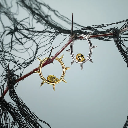 Silver and gold Memento Skull hoop earrings hanging from a dark branch