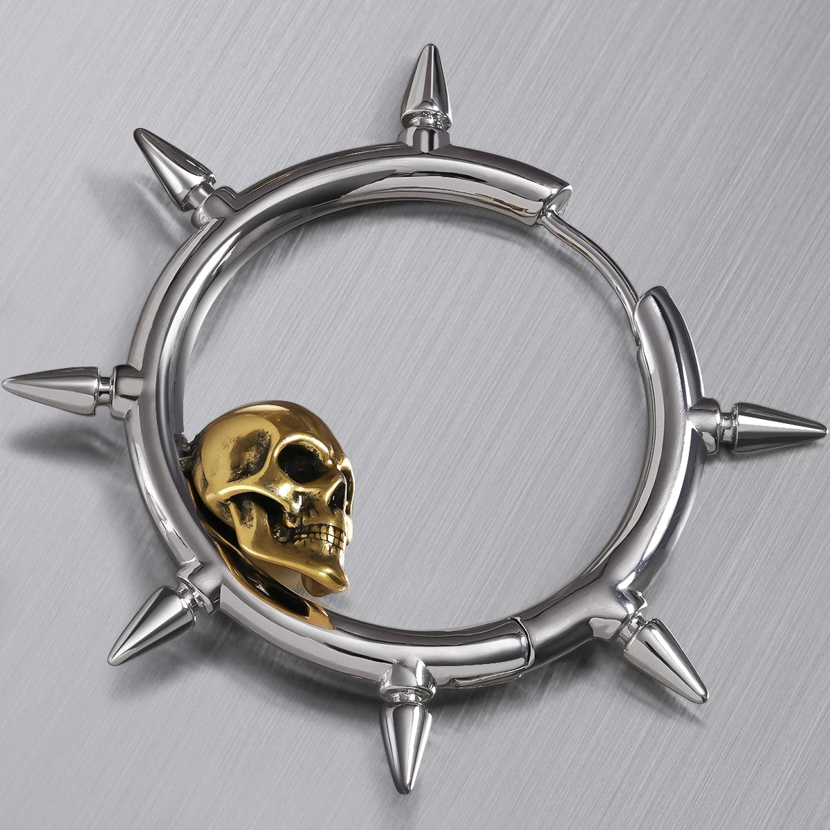 Close-up top view of a silver-tone spiked hoop earring with a gold-tone skull resting inside the ring