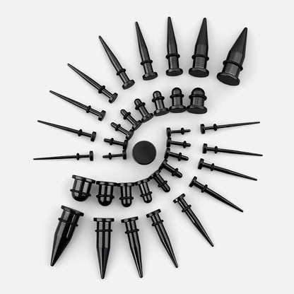 Black stainless steel ear tapers of various gauges arranged in a spiral pattern on a light background