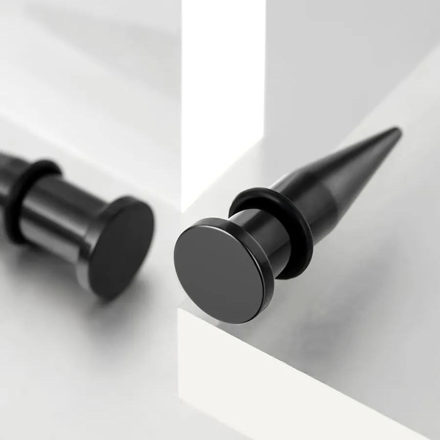 Two black stainless steel ear tapers with rubber o-rings resting on a light surface, close view