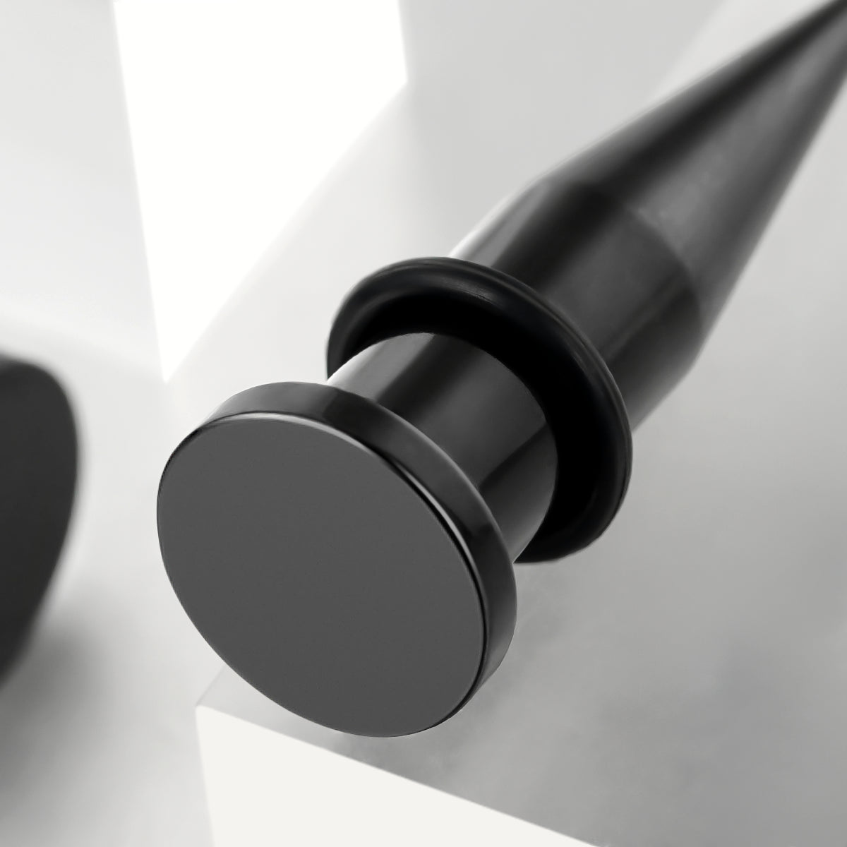 Angled close-up of a black stainless steel ear taper showing tapered point and o-ring detail