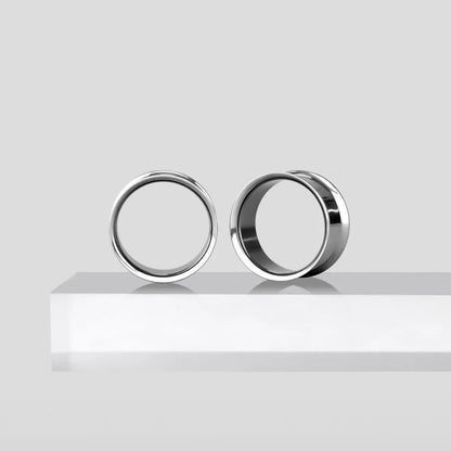 Two titanium loop tunnels resting side by side on a white ledge, one facing forward